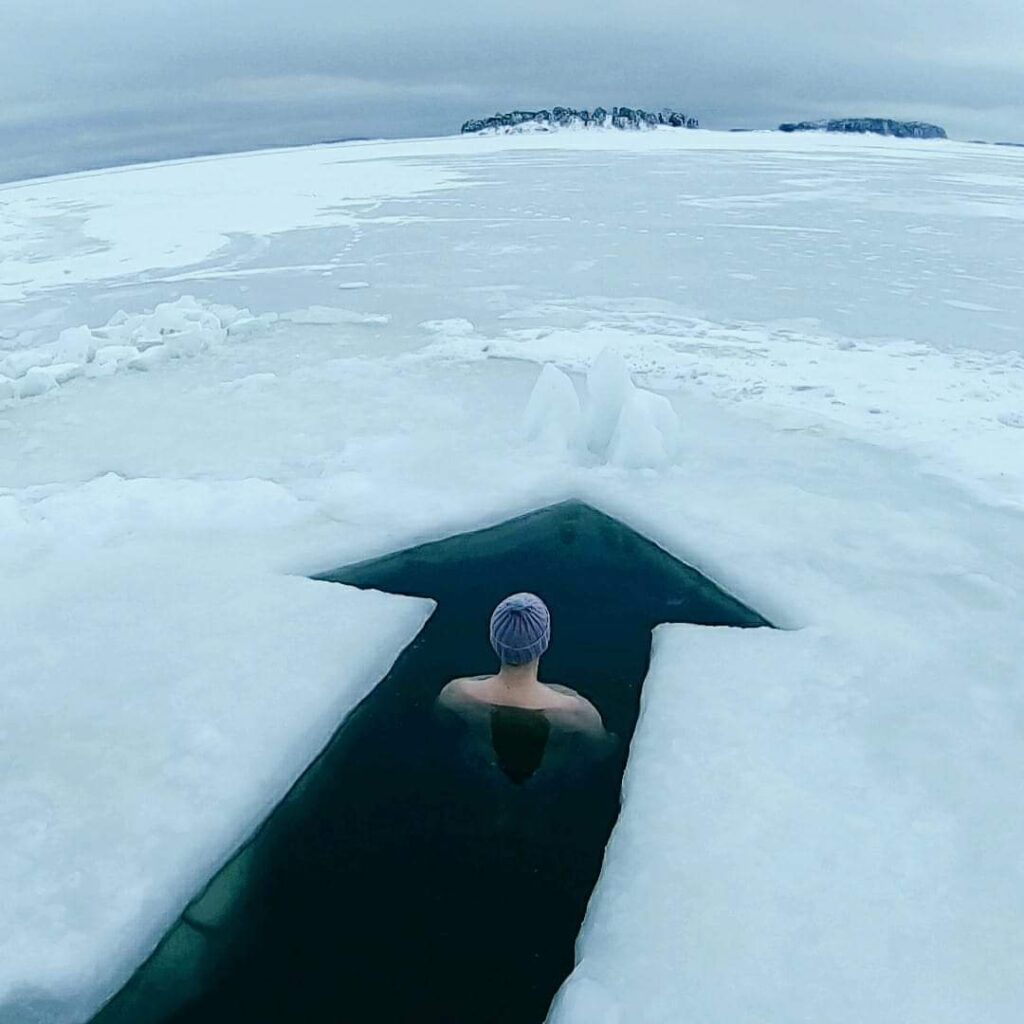 Henkilö istuu avannossa jääkentän keskellä talvimaisemassa – pysähtymisen ja luottamuksen hetki uudenvuodenlupauksen tueksi