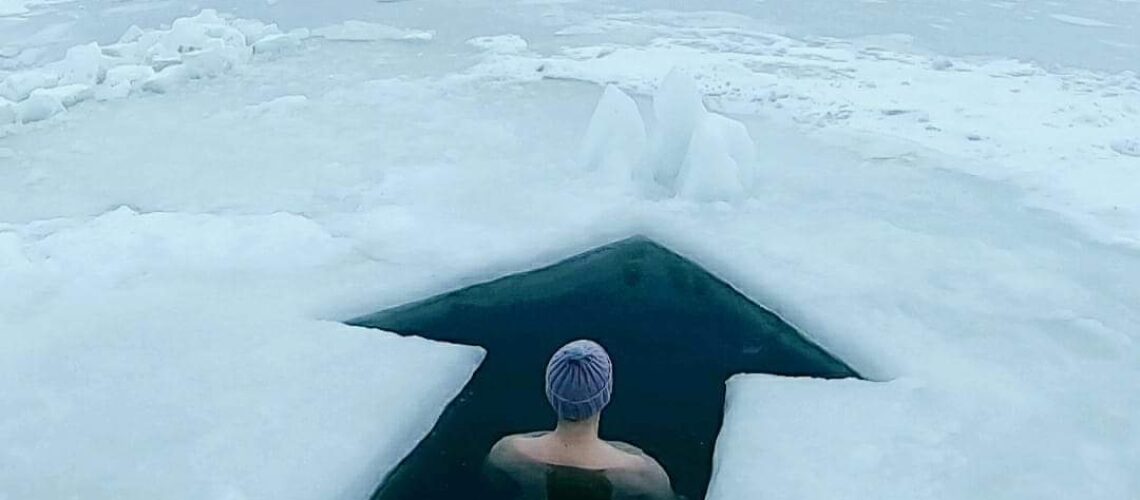 Henkilö istuu avannossa jääkentän keskellä talvimaisemassa – pysähtymisen ja luottamuksen hetki uudenvuodenlupauksen tueksi